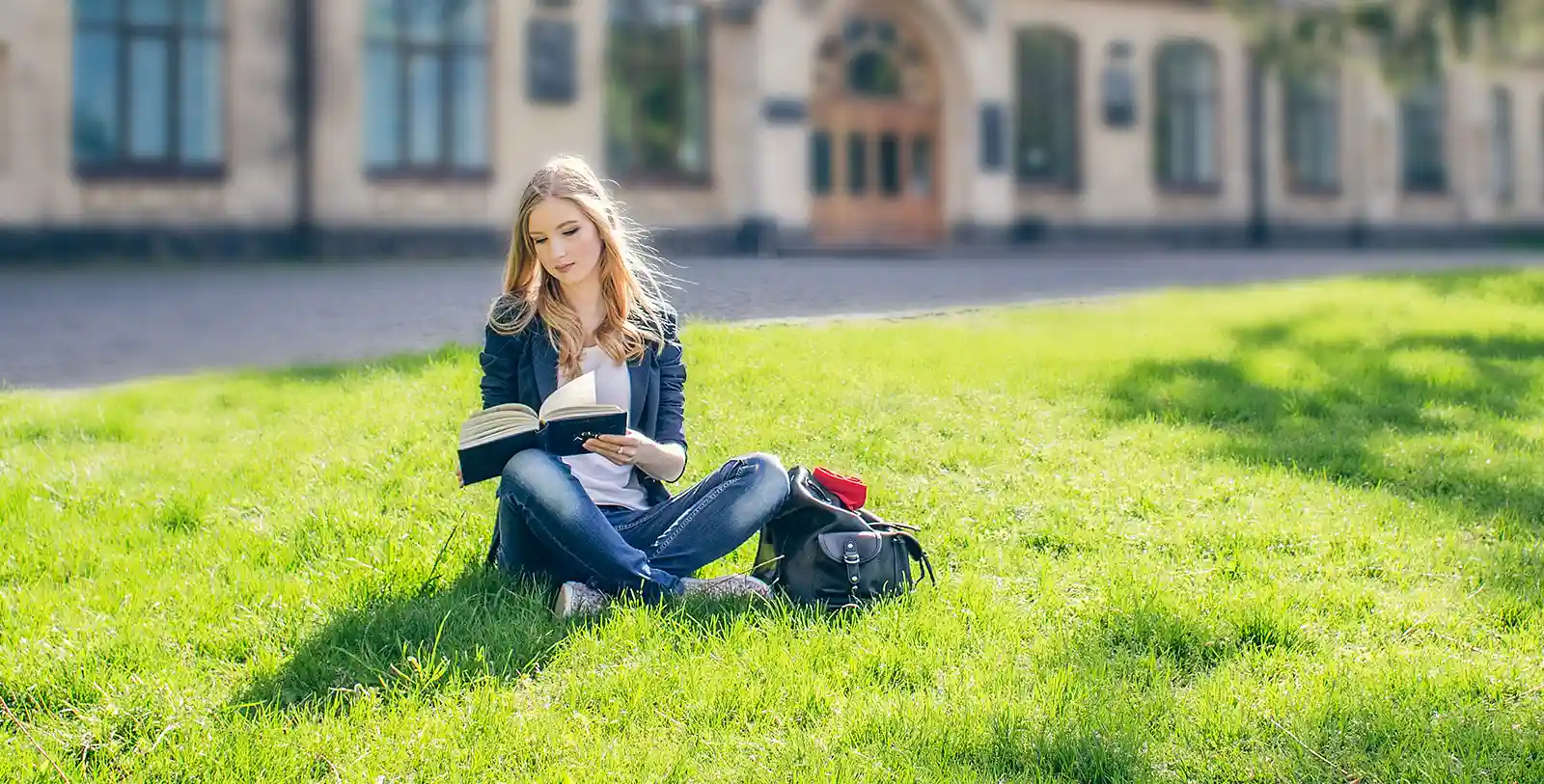 A young lady is studying while sitting on the grass of the green space in a university in Istanbul